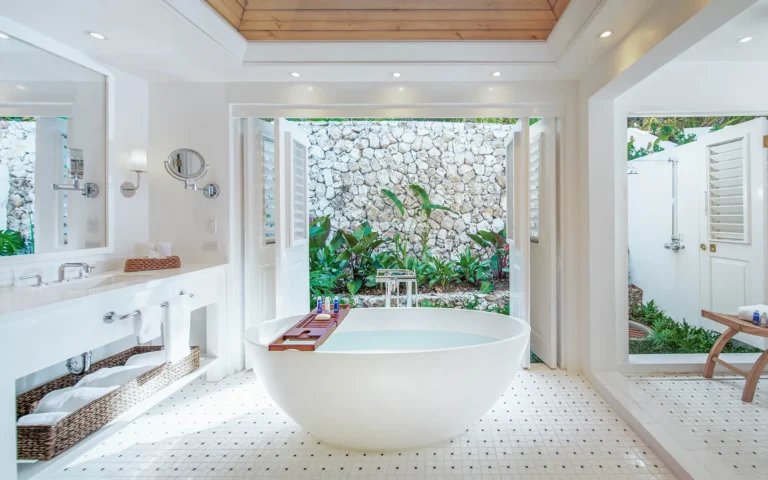 Freestanding white tub in a villa bathroom opening onto a stone-walled outdoor shower court
