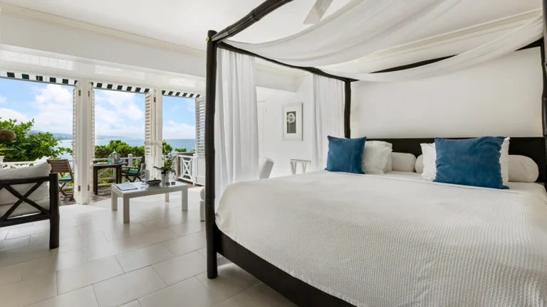 Four-poster king bed with white curtains and balcony doors opening to the sea
