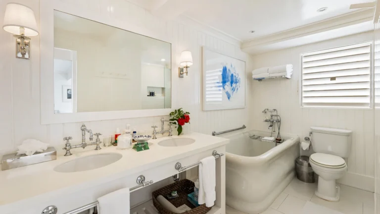 Double vanity, white bathtub and louvred window in a hotel room bathroom