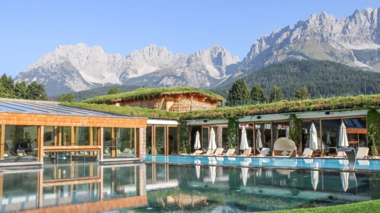 Outdoor saltwater pool in front of a grass-roofed glass pavilion, sun loungers and the Wilder Kaiser peaks