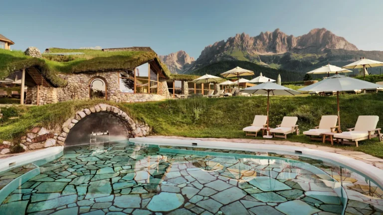 Flagstone-floored outdoor pool beneath a grass-roofed stone grotto with sun loungers and parasols