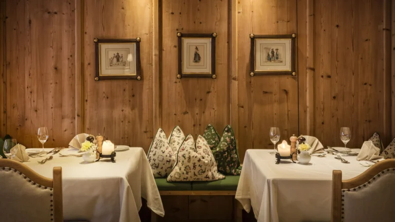 Panelled dining nook with a green bench, patterned cushions and two laid tables with candles