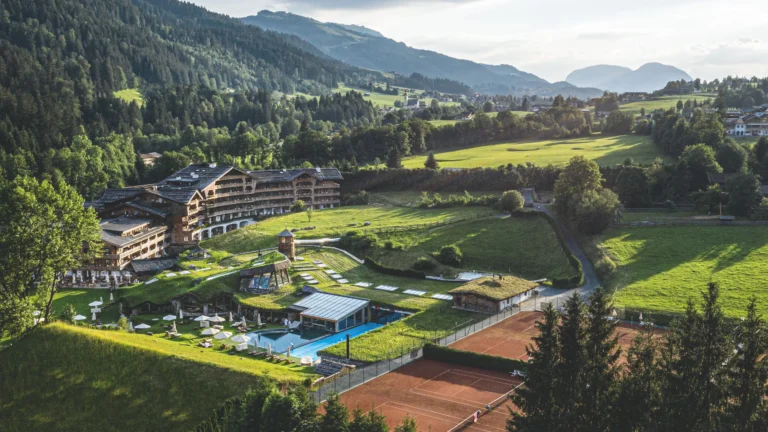 Aerial view of the resort with a long timber hotel wing, garden pools, grass-roofed pavilions and tennis courts in a green valley